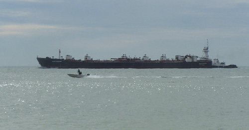 A tug boat pushing a barge while a small pleasure boat passes beside it.
